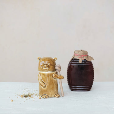 Brown stoneware bear honey jar holding a wooden honey dipper