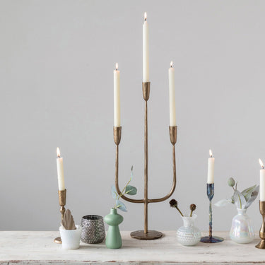 Lit taper candles in assorted hand-forged metal holders on a styled tabletop
