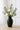 Charcoal ceramic tall vase with matte finish, styled with ivory ranunculus and eucalyptus stems on a light wood table.
