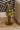 A gold-toned rabbit figurine standing behind a tray filled with green moss, small eggs, and a glass vase with dried stems, placed on a wooden floor next to a beige upholstered chair.