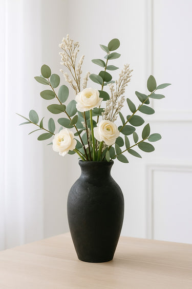 Charcoal ceramic tall vase with matte finish, styled with ivory ranunculus and eucalyptus stems on a light wood table.