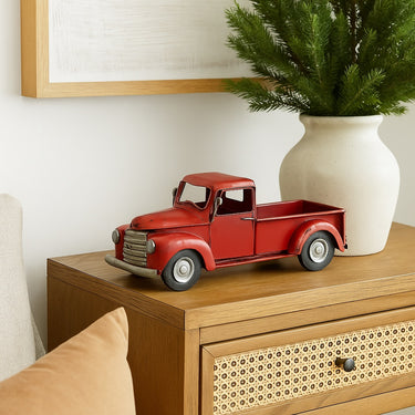 Vintage-style red metal truck decor on a wooden cabinet, styled next to a cream ceramic vase with greenery in a cozy living space.