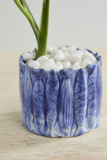Close-up of blue hand-painted ceramic sardine pot with raised fish texture and white stones
