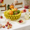 Glossy yellow ceramic banana fruit bowl with dimensional banana details, styled as a colorful kitchen centerpiece with fresh fruit and florals.