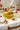 Glossy yellow ceramic banana fruit bowl with dimensional banana details, styled as a colorful kitchen centerpiece with fresh fruit and florals.