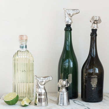Three bottles with unique silver animal-shaped bottle stoppers on a white surface.