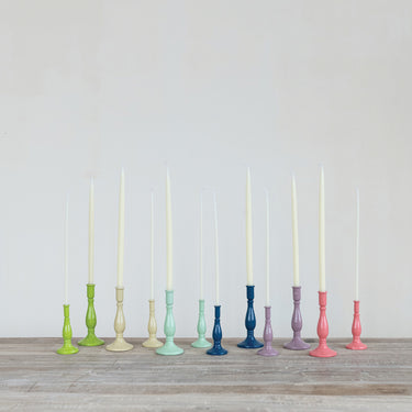 Set of colorful cast iron taper candle holders with slim white taper candles displayed on a wooden surface