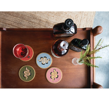 • Glass beaded coaster with snake design under a drink glass on a wooden tray