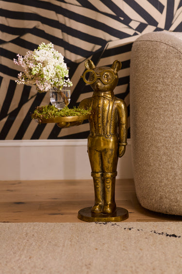Bronze statue of a figure with a tray holding flowers against a zebra-striped wall.