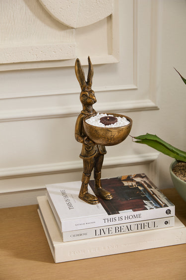 Brass-gold metal E+E Eric Hare dish stand holding a small decorative bowl, styled as a whimsical storybook-inspired tabletop accent