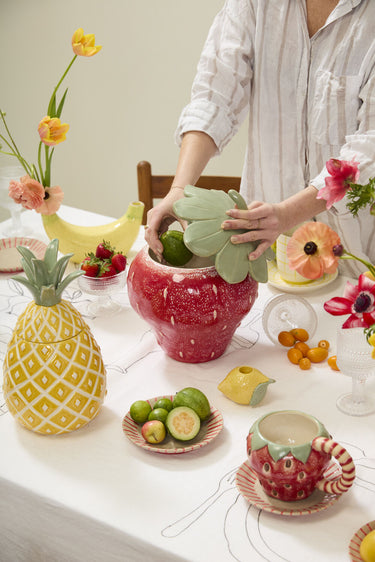 Food-safe ceramic strawberry canister cookie jar with removable green stem lid, dimensional seed details, and glossy red reactive glaze for colorful kitchen decor.