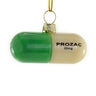 Cody Foster Stress Free Pill glass ornament shaped like a green and cream capsule with black printed lettering, gold cap, and gold hanging cord.