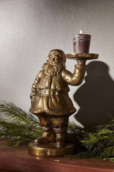 Saint Nick metal figurine holding a small candle styled with holiday greenery on a mantel