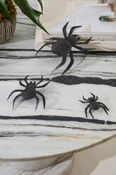 Set of three black metal spiders styled on a marble tabletop with books and greenery